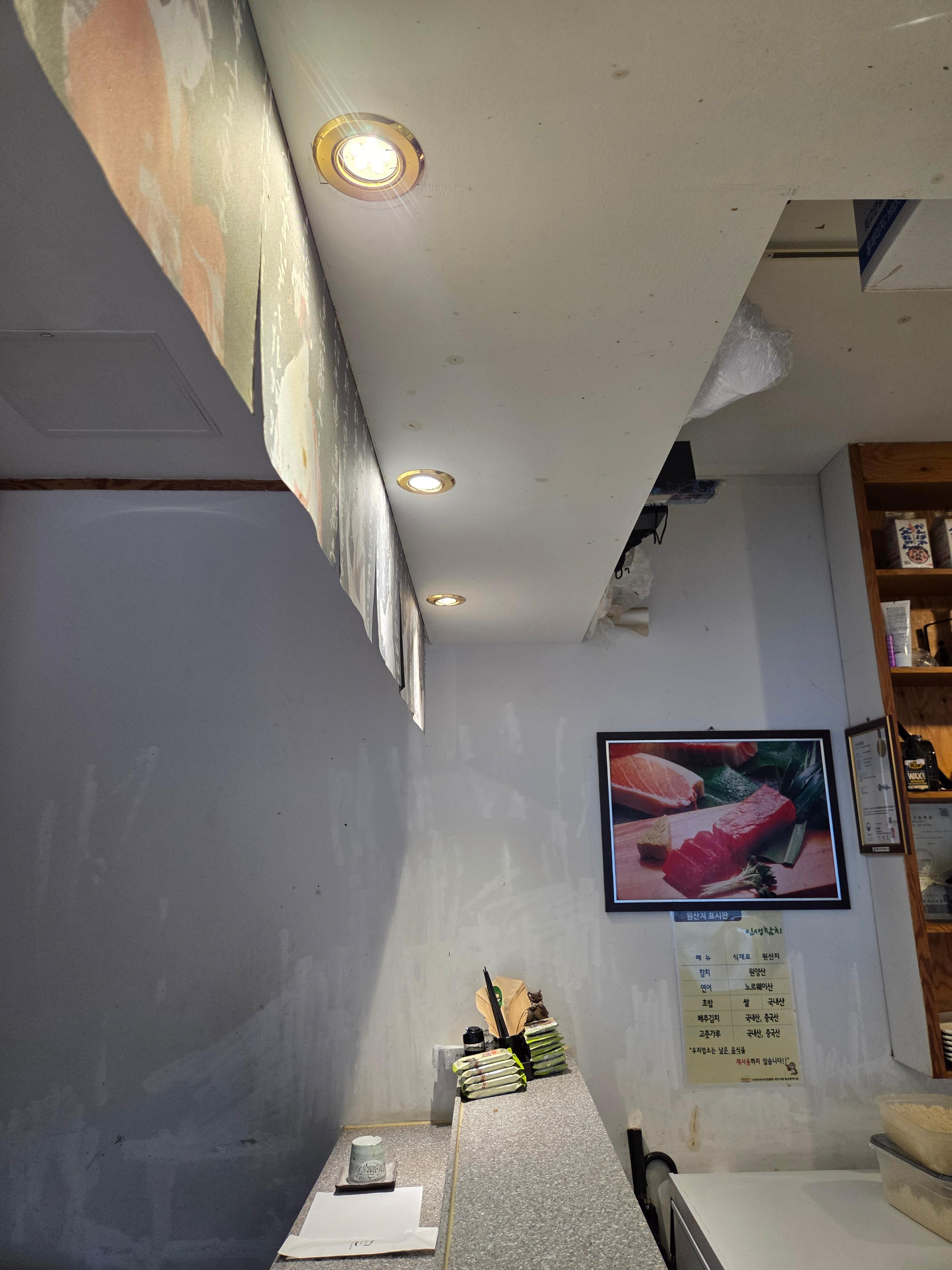 음식점 카운터 위 천장에 금색 테두리의 둥근 매입등이 켜진 모습
